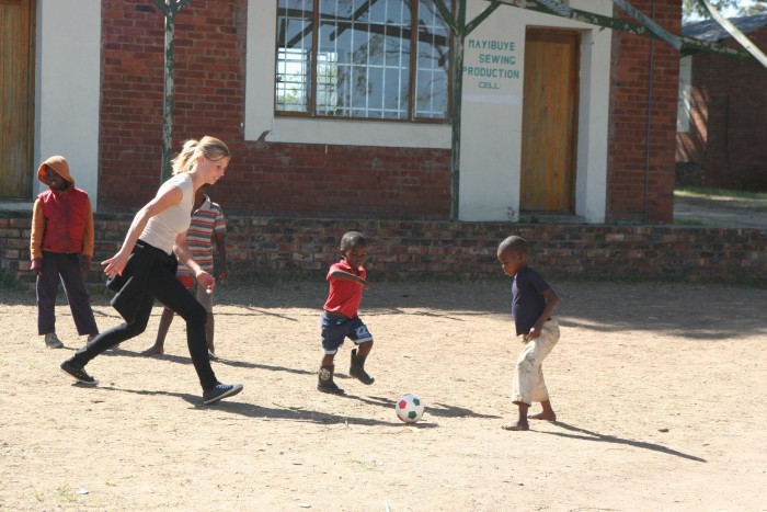 A volunteer kicking a ball with local school children