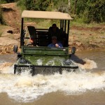 Game rangers travel across a stream in the jeep with volunteers