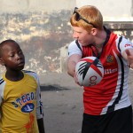 A volunteer instructs a young boy how to pass a rugby ball