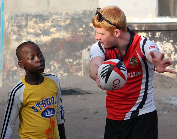 A volunteer instructs a young boy how to pass a rugby ball
