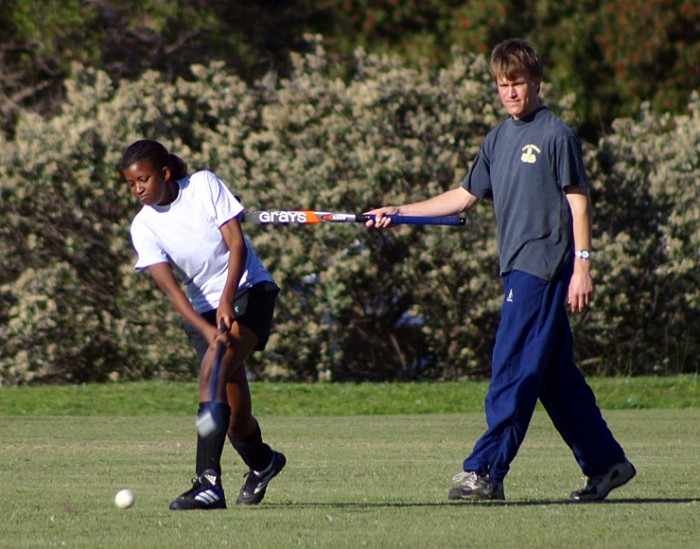 A volunteer helps an African girl with her striking technique in hockey